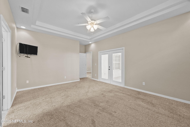 unfurnished room with a raised ceiling, carpet flooring, ceiling fan, and french doors