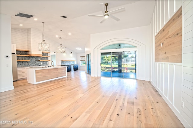 kitchen with lofted ceiling, light hardwood / wood-style flooring, pendant lighting, a kitchen island with sink, and decorative backsplash