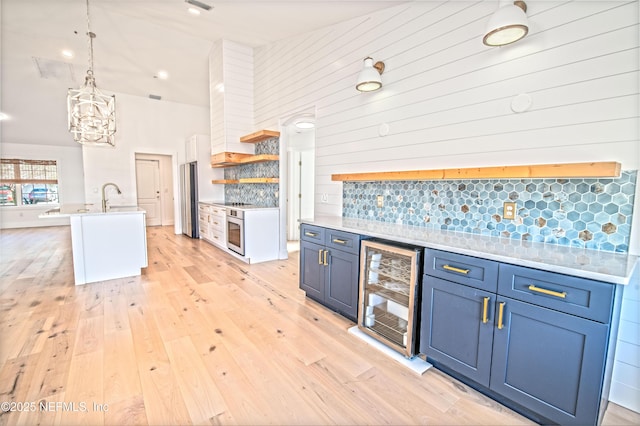 kitchen with blue cabinets, tasteful backsplash, a center island with sink, light wood-type flooring, and beverage cooler