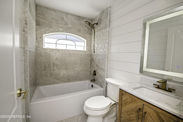 full bathroom featuring tiled shower / bath, toilet, vanity, and wood walls