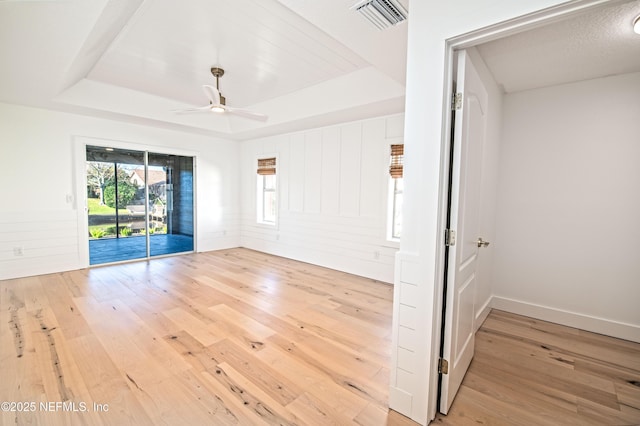 empty room featuring ceiling fan, a tray ceiling, and light hardwood / wood-style flooring