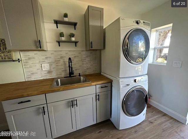 laundry area featuring cabinets, sink, stacked washer and dryer, and light hardwood / wood-style floors