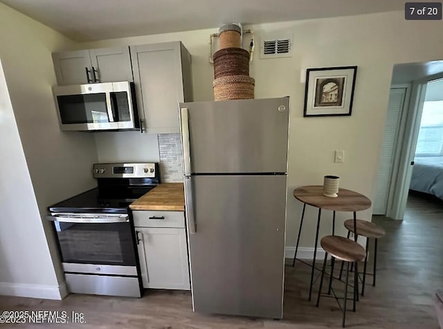 kitchen with gray cabinets, dark wood-type flooring, butcher block counters, and stainless steel appliances