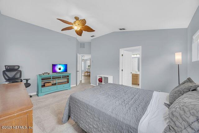 bedroom featuring vaulted ceiling, connected bathroom, light colored carpet, and ceiling fan