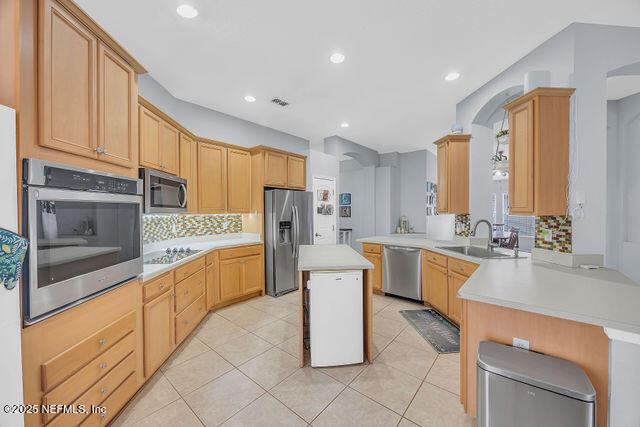 kitchen with sink, backsplash, stainless steel appliances, a kitchen island, and kitchen peninsula