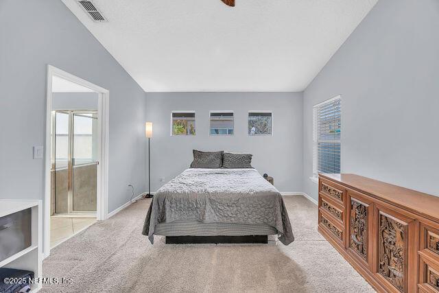 bedroom with ensuite bath, vaulted ceiling, and light carpet