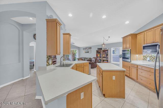 kitchen with vaulted ceiling, appliances with stainless steel finishes, sink, a center island, and kitchen peninsula