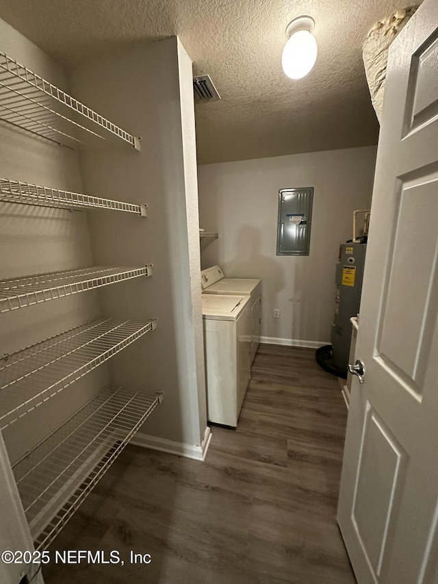 laundry room with electric panel, dark wood-type flooring, washing machine and clothes dryer, a textured ceiling, and water heater