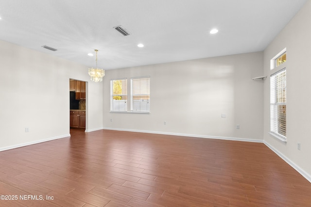 empty room with a notable chandelier, dark wood-type flooring, and a healthy amount of sunlight