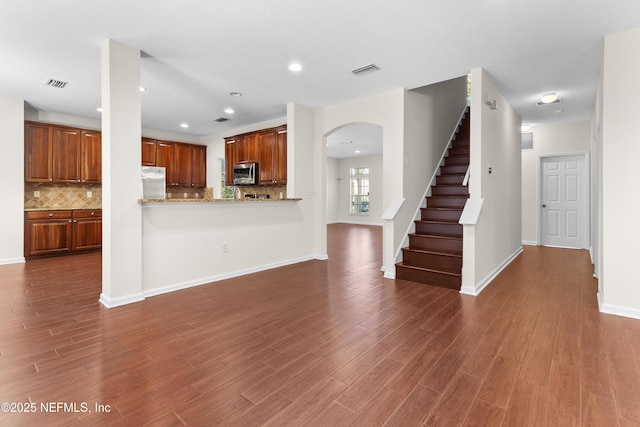 kitchen featuring backsplash, stainless steel appliances, light stone countertops, dark hardwood / wood-style flooring, and kitchen peninsula