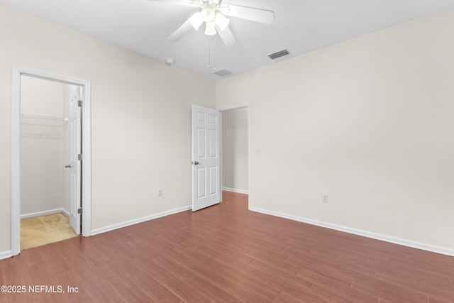 unfurnished bedroom with hardwood / wood-style flooring, a walk in closet, ceiling fan, and a closet