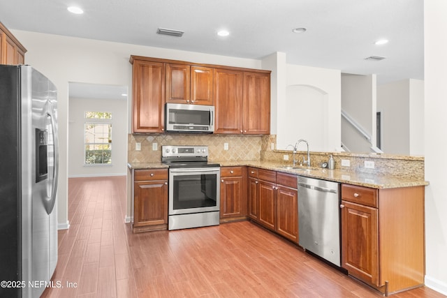 kitchen featuring appliances with stainless steel finishes, tasteful backsplash, sink, light stone counters, and light hardwood / wood-style floors