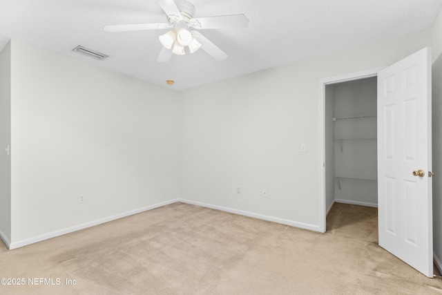 unfurnished bedroom featuring a walk in closet, light carpet, ceiling fan, and a closet