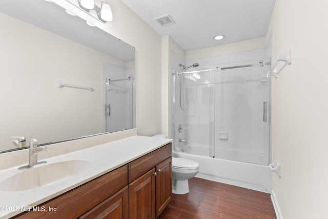 full bathroom with vanity, combined bath / shower with glass door, a textured ceiling, and toilet