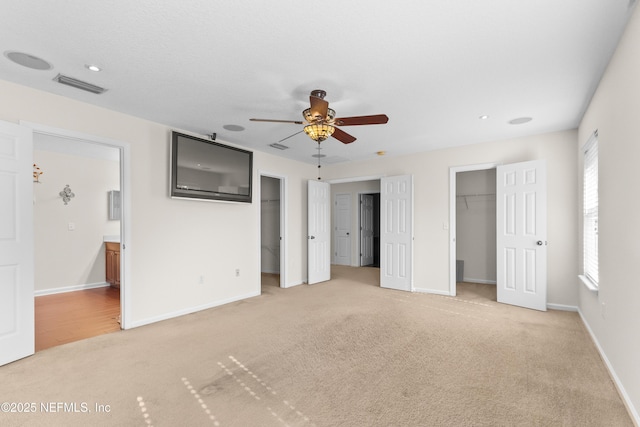 unfurnished bedroom with ceiling fan, connected bathroom, light carpet, and a walk in closet