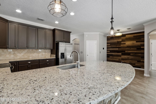 kitchen featuring stainless steel fridge with ice dispenser, sink, hanging light fixtures, and wood walls