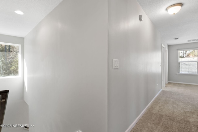 hallway with light carpet and a textured ceiling