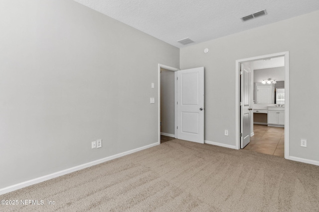 unfurnished bedroom with ensuite bath, light colored carpet, and a textured ceiling