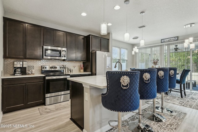 kitchen featuring a breakfast bar, a center island with sink, light countertops, backsplash, and appliances with stainless steel finishes