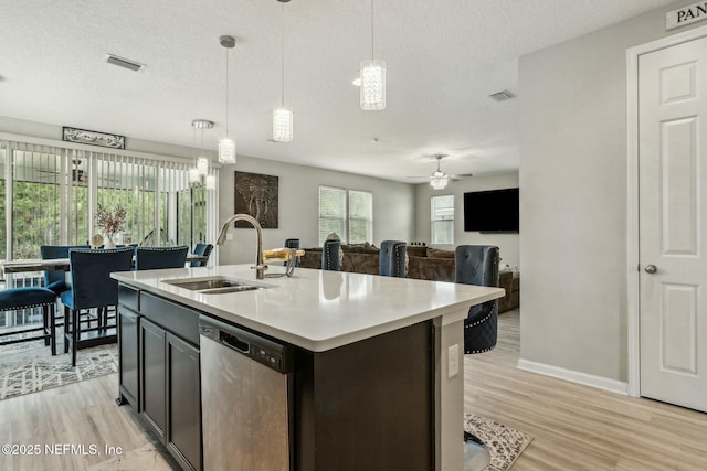 kitchen featuring a textured ceiling, a sink, light wood-style floors, light countertops, and stainless steel dishwasher