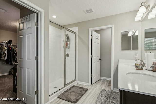 bathroom with a textured ceiling, a sink, visible vents, and a shower stall