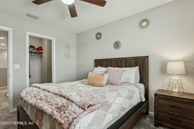 carpeted bedroom featuring visible vents, a ceiling fan, a walk in closet, a textured ceiling, and a closet