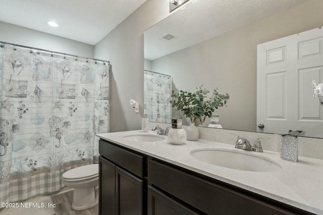 bathroom featuring toilet, double vanity, a sink, and visible vents