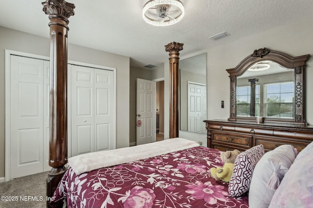 bedroom with a textured ceiling, carpet, two closets, and visible vents