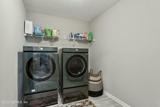 laundry area featuring laundry area, baseboards, wood finished floors, washing machine and clothes dryer, and a textured ceiling