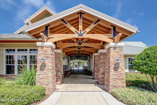 doorway to property featuring stone siding, metal roof, a standing seam roof, and a gate