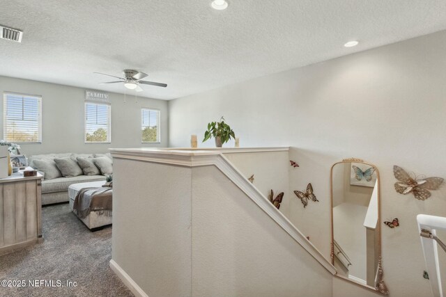 hall with visible vents, a textured ceiling, an upstairs landing, carpet floors, and recessed lighting