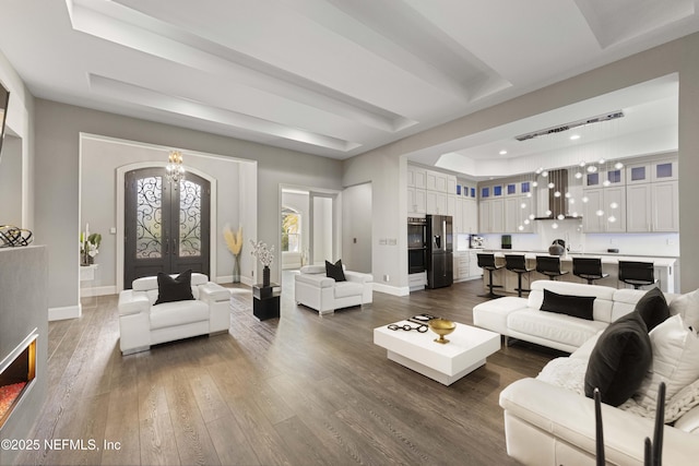 living room featuring an inviting chandelier, a tray ceiling, dark wood-type flooring, and french doors