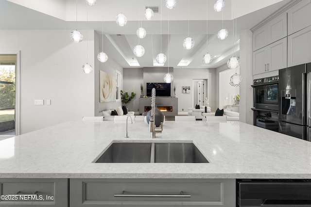 kitchen with sink, gray cabinets, a kitchen island with sink, black appliances, and light stone countertops