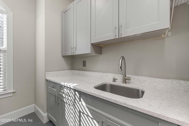 kitchen with light stone counters, sink, and gray cabinets