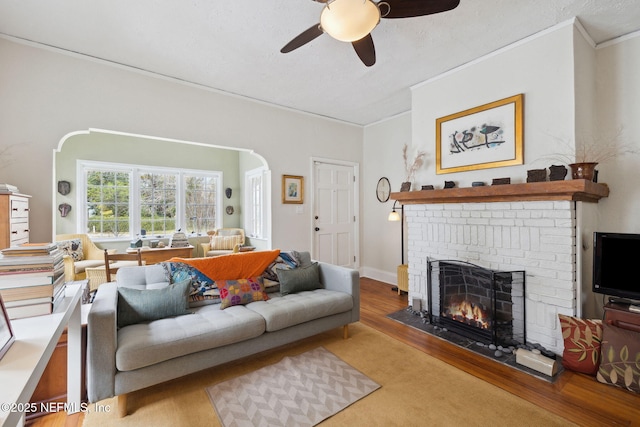 living room featuring crown molding, a brick fireplace, a textured ceiling, ceiling fan, and hardwood / wood-style floors