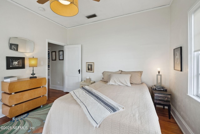 bedroom featuring dark wood-type flooring, ceiling fan, ornamental molding, and multiple windows