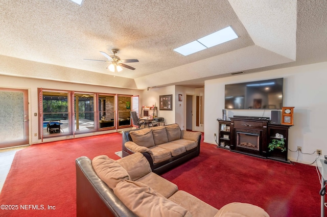 carpeted living room with ceiling fan, a tray ceiling, a skylight, and a textured ceiling