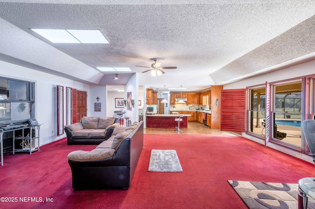 carpeted living room featuring vaulted ceiling with skylight, a textured ceiling, and ceiling fan