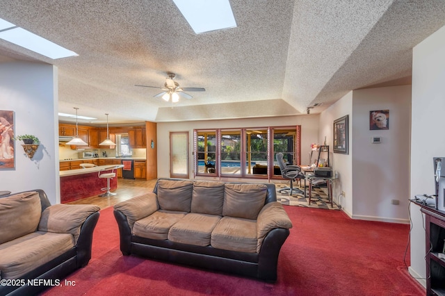 carpeted living room with a raised ceiling, ceiling fan, and a skylight