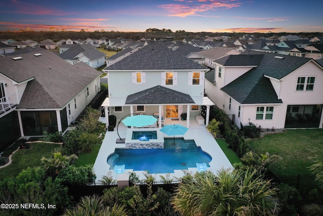 back house at dusk featuring a pool with hot tub and a patio area