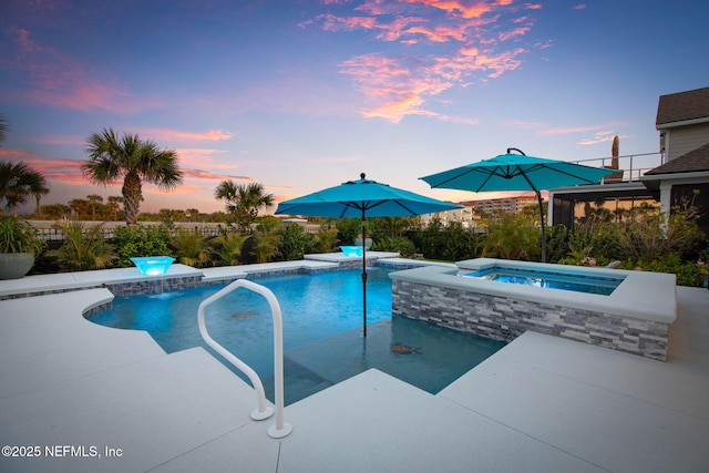 pool at dusk featuring an in ground hot tub and a patio area