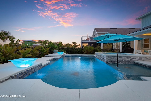 pool at dusk with an in ground hot tub, pool water feature, and a patio