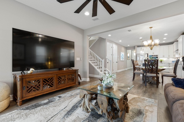 living room featuring ceiling fan with notable chandelier and light wood-type flooring