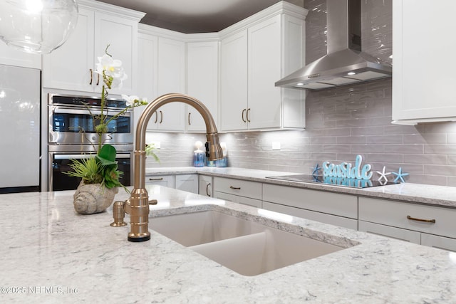 kitchen featuring white cabinetry, light stone counters, stainless steel double oven, and wall chimney exhaust hood