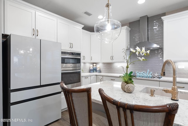 kitchen featuring white cabinetry, light stone countertops, a kitchen bar, wall chimney exhaust hood, and white fridge