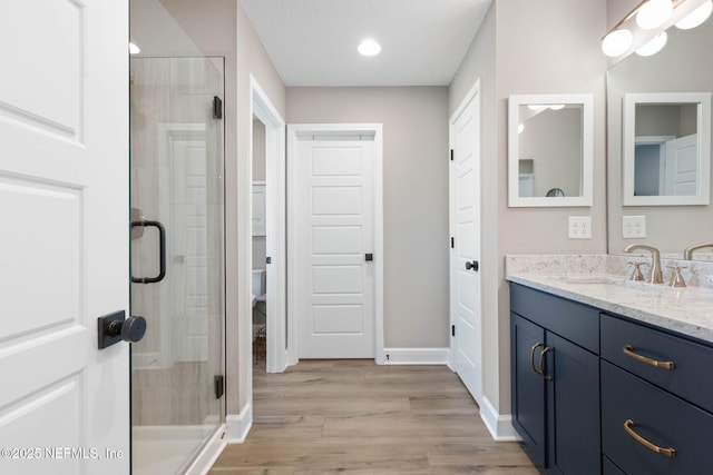 bathroom with a shower with shower door, hardwood / wood-style flooring, vanity, toilet, and a textured ceiling