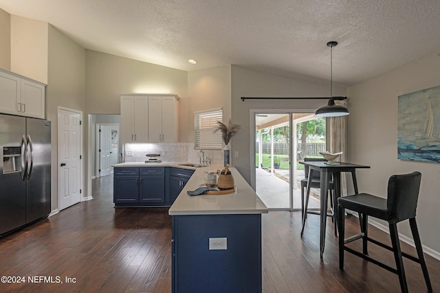 kitchen with pendant lighting, blue cabinets, sink, white cabinets, and stainless steel fridge