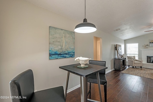 dining area with vaulted ceiling, dark hardwood / wood-style floors, a fireplace, ceiling fan, and a textured ceiling