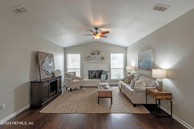 living room featuring vaulted ceiling, dark hardwood / wood-style floors, a fireplace, ceiling fan, and a textured ceiling