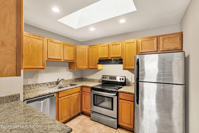 kitchen featuring sink, appliances with stainless steel finishes, a skylight, light stone counters, and light tile patterned flooring